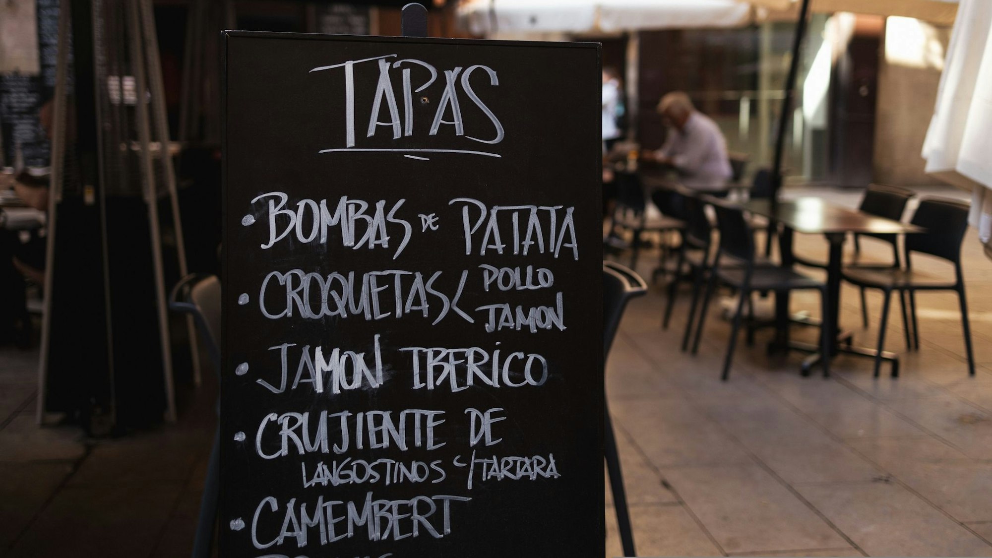 Tapas-Tafel mit Menükarte und Außengastronomie im Hintergrund.