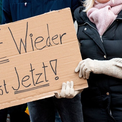 Teilnehmer einer Demonstration gegen Rechtsextremismus halten ein Schild „Nie wieder ist jetzt" in Händen.