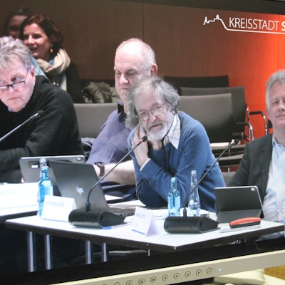Ein Mann an einem Mikrophon an seinem Tisch in einem Ratsaal