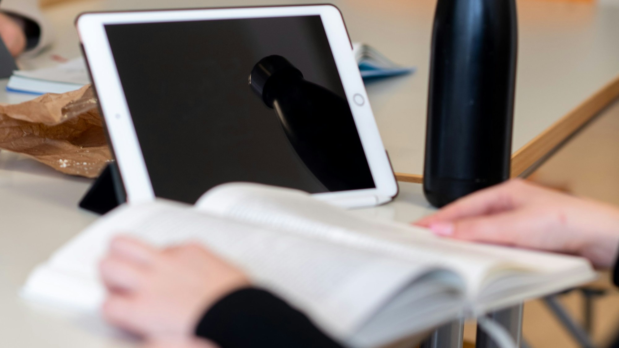 Das Bild zeigt eine Schülerin, die in einem Buch liest. Hinter dem Buch steht ein Tablet.