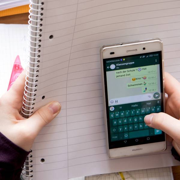Eine Schülerin sitzt mit ihrem Handy und ihren Schulsachen an einem Schreibtisch.