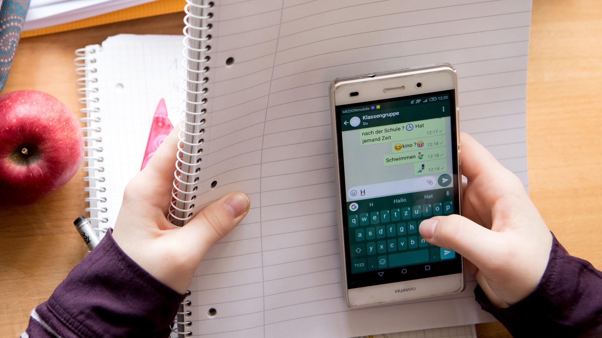 Eine Schülerin sitzt mit ihrem Handy und ihren Schulsachen an einem Schreibtisch.