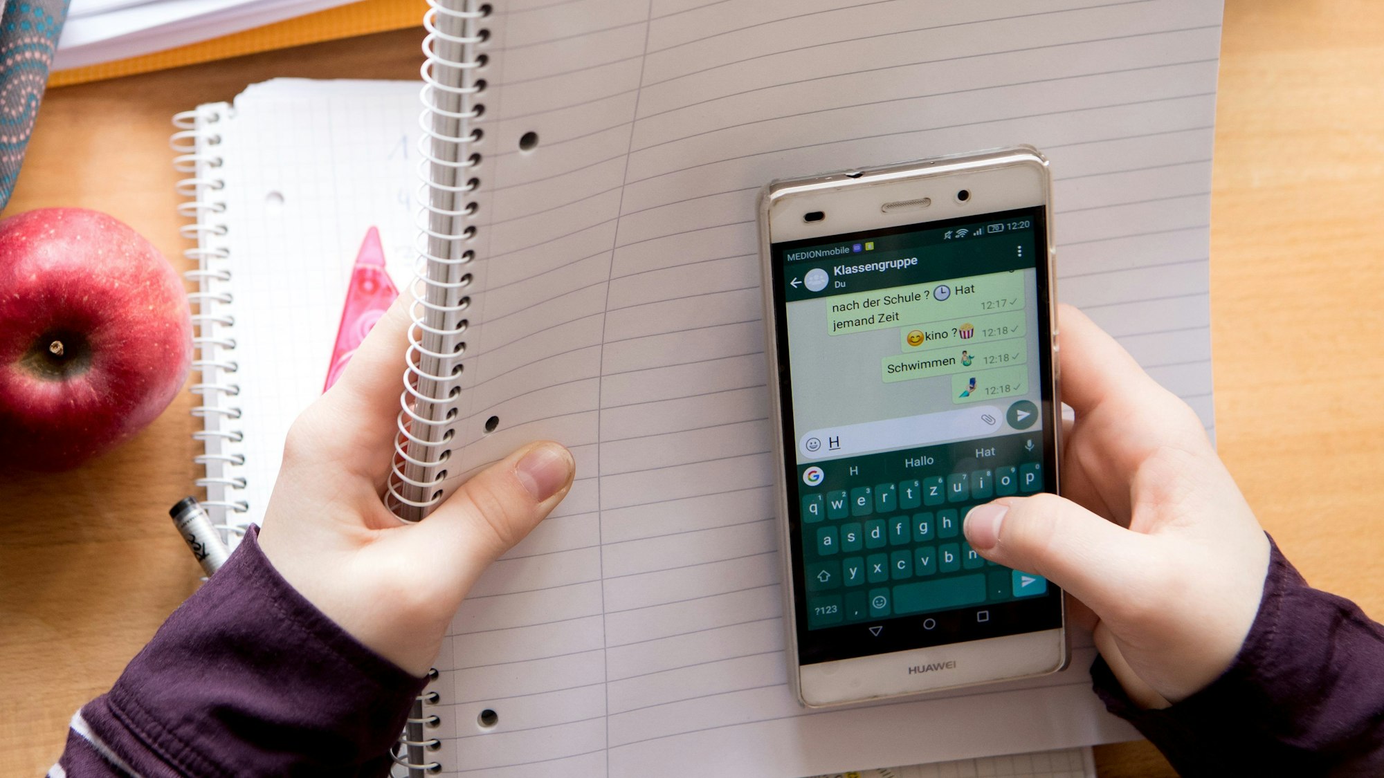 Eine Schülerin sitzt mit ihrem Handy und ihren Schulsachen an einem Schreibtisch.