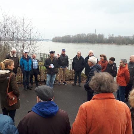 Menschen stehen im Halbkreis direkt am Rheinufer.