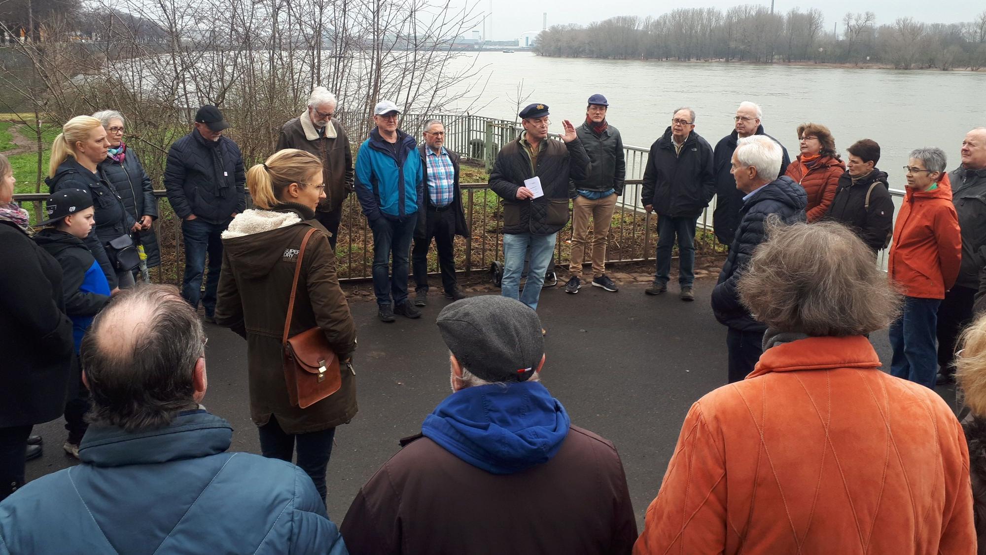 Menschen stehen im Halbkreis direkt am Rheinufer.