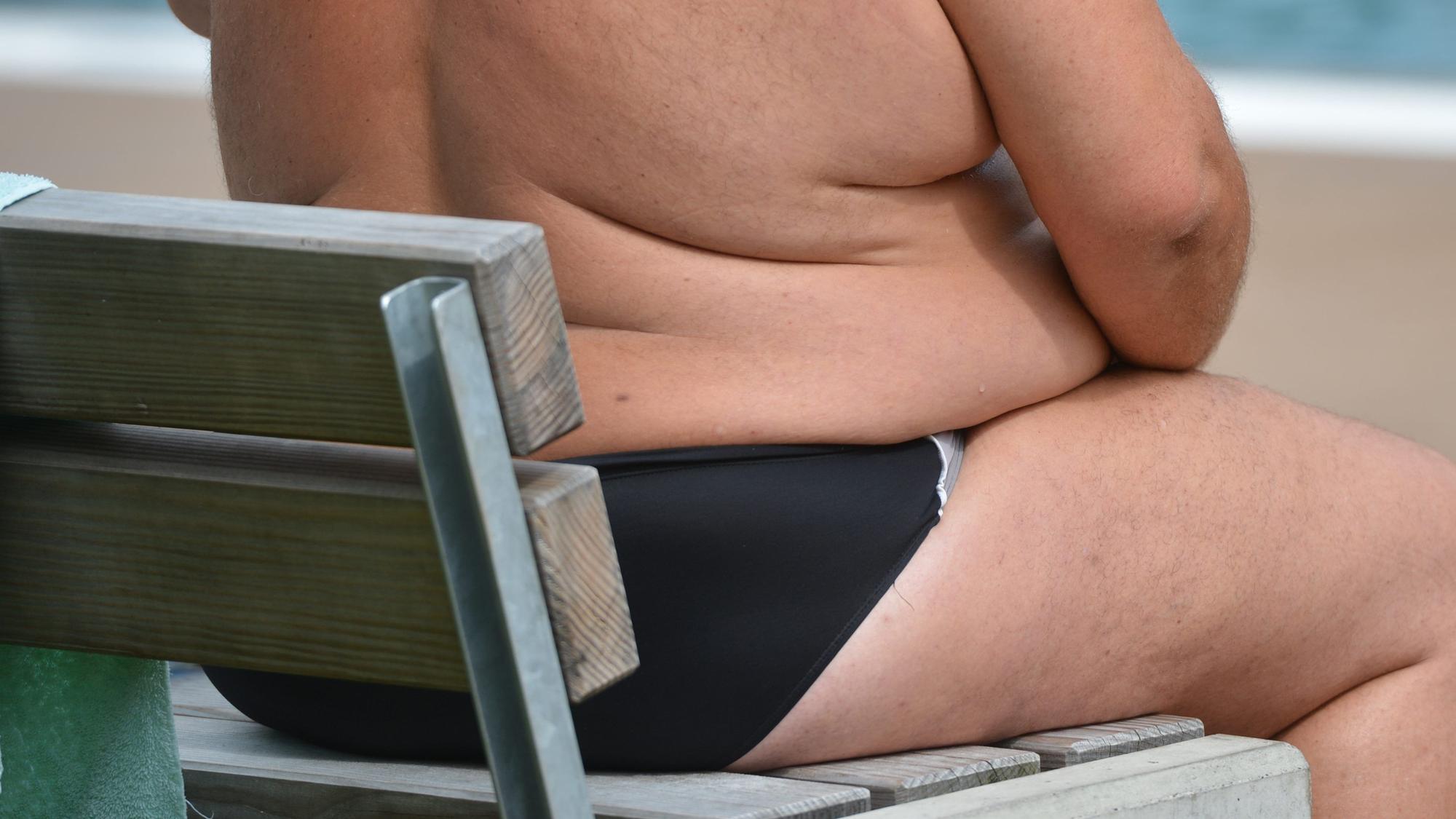 Ein übergewichtiger Mann sitzt in einem Freibad.