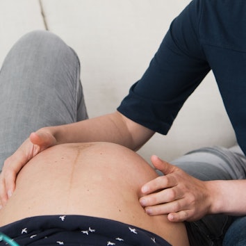 Eine Hebamme tastet den Bauch einer Frau ab, die im neunten Monat ist.