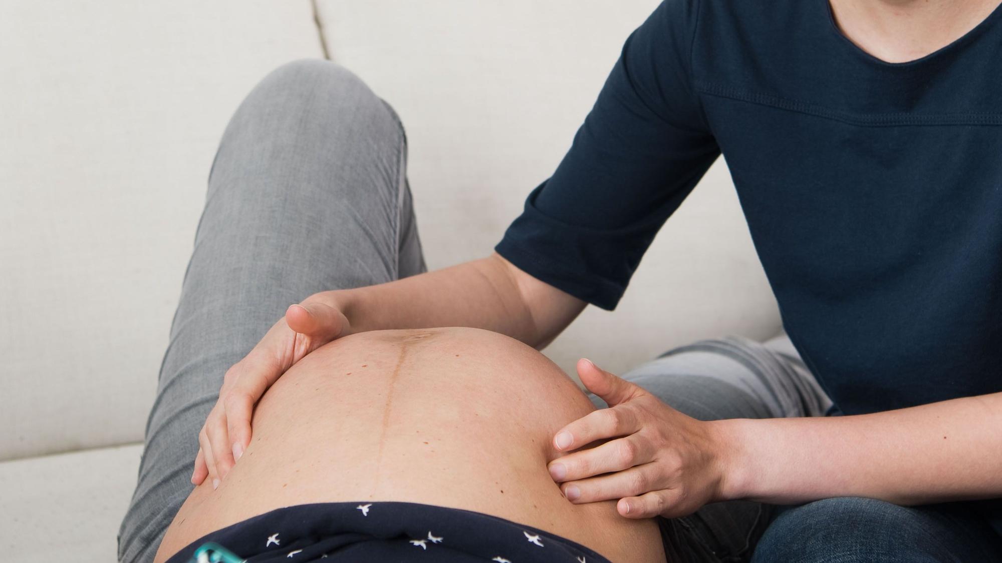 Eine Hebamme tastet den Bauch einer Frau ab, die im neunten Monat ist.