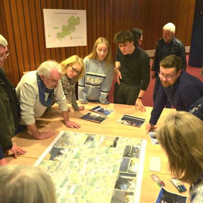 Mehrere Leute stehen um einen Stadtplan herum, der auf einem Tisch liegt.