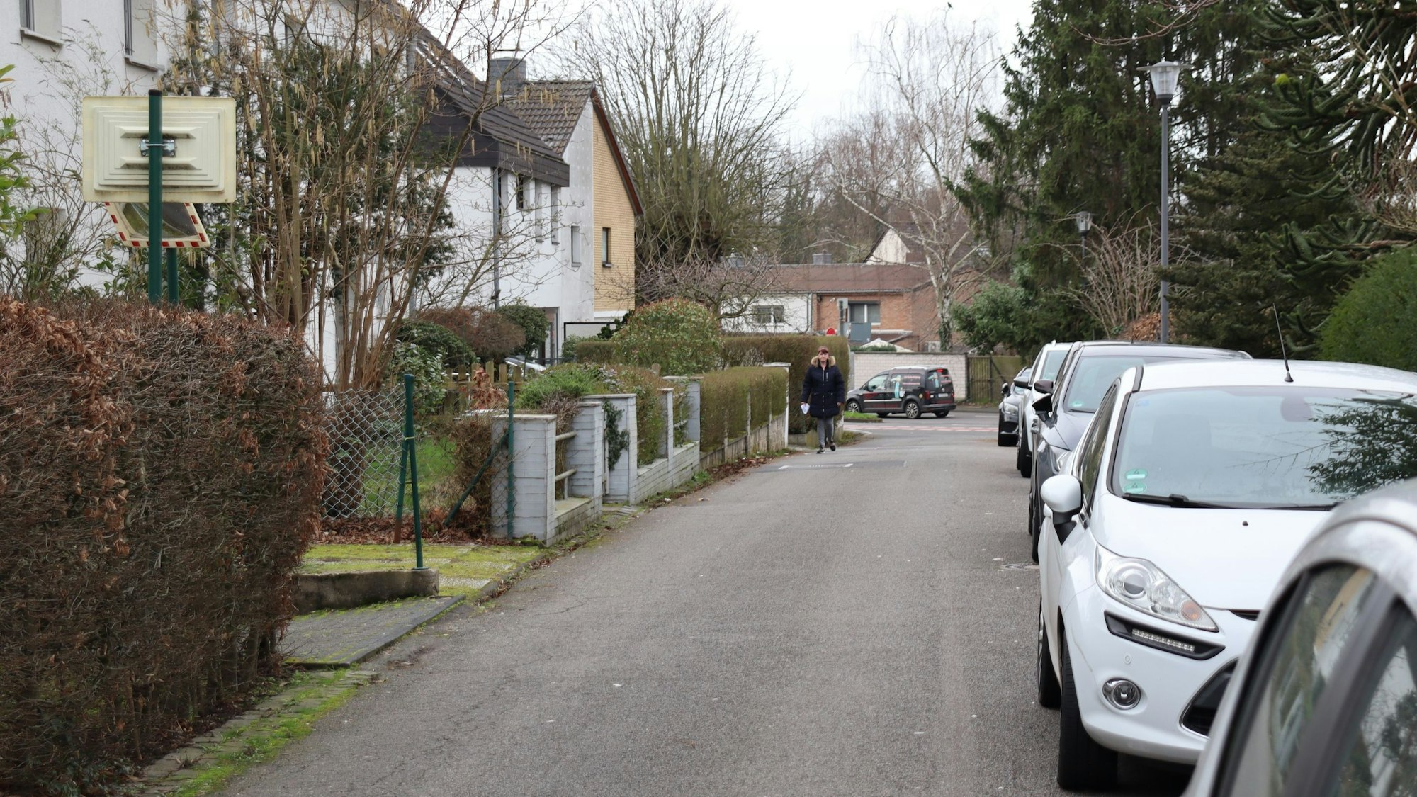 Eine schmale Wohnstraße mit parkenden Autos am Straßenrand ist zu sehen.