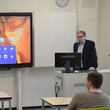 Zu sehen ist ein Mann neben einer digitalen Tafel.