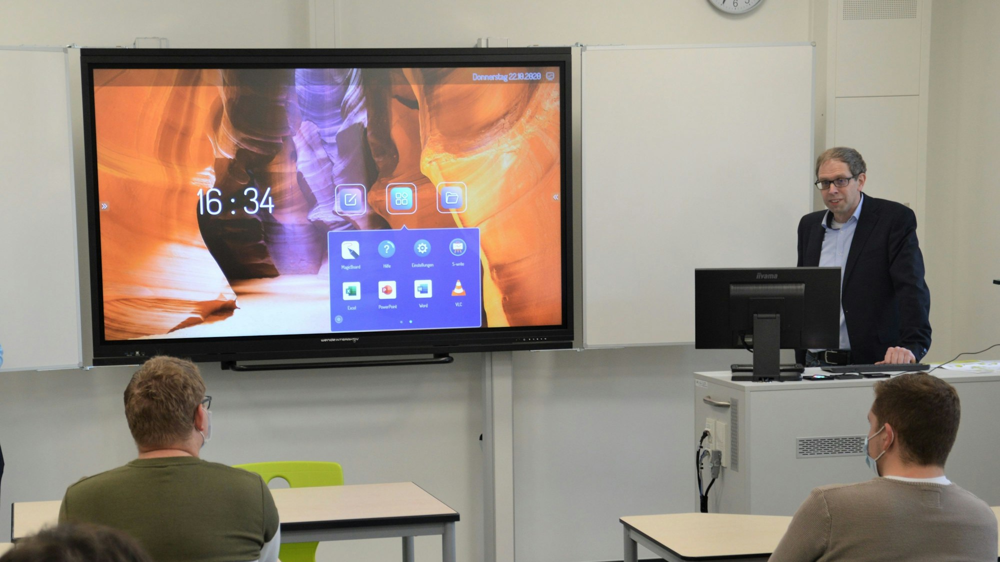 Zu sehen ist ein Mann neben einer digitalen Tafel.