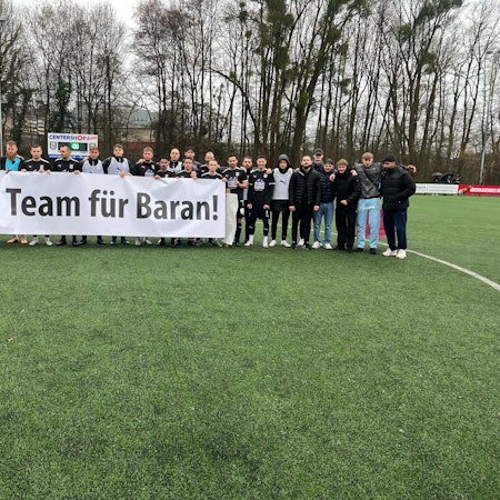 Die Spieler des SSV Jan Wellem halten ein Banner mit der Aufschrift "Als Team für Baran!" hoch