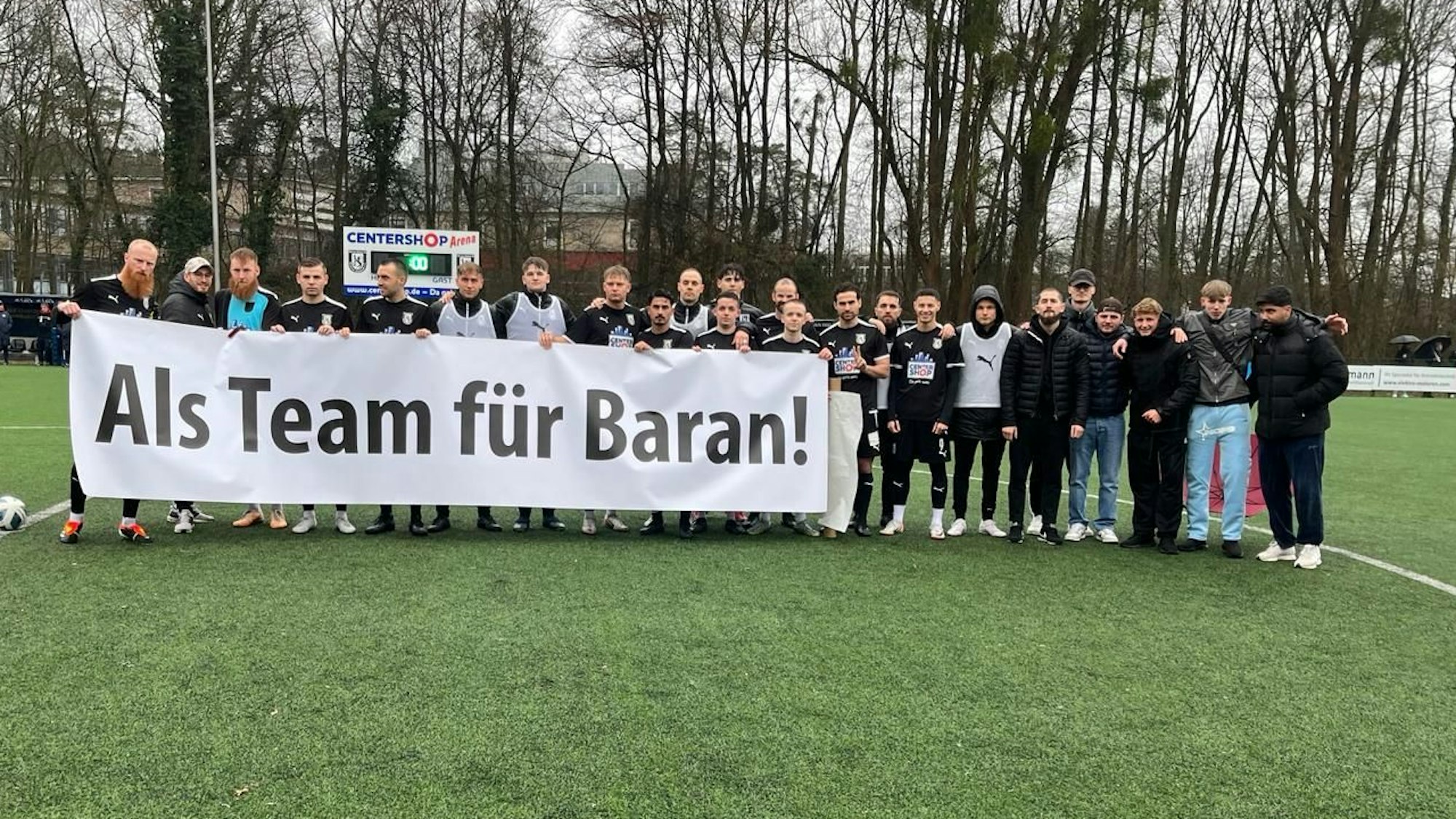 Die Spieler des SSV Jan Wellem halten ein Banner mit der Aufschrift "Als Team für Baran!" hoch