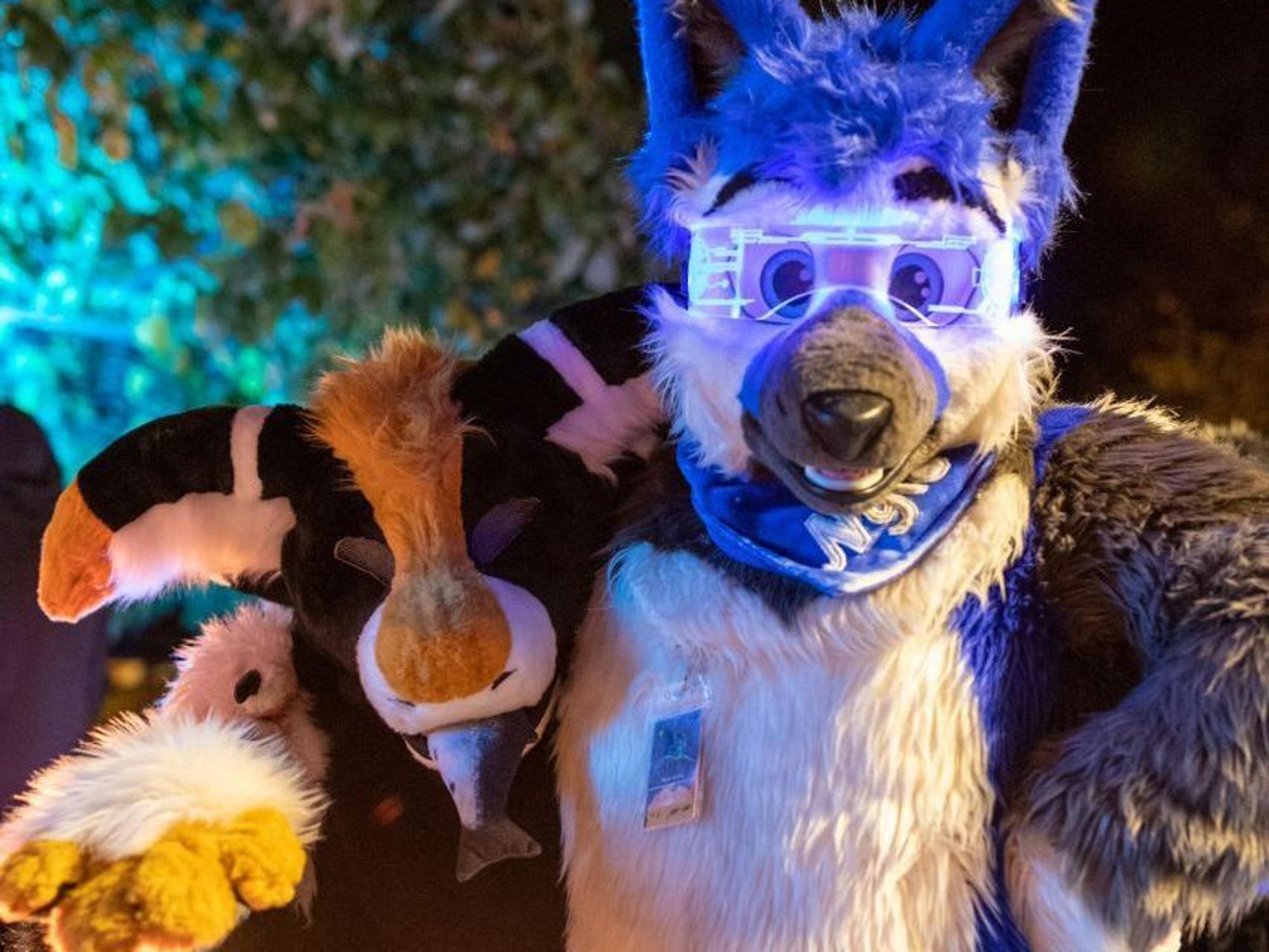 Ein plüschiger Manokin und ein plüschiger Wolf, der eine LED-Sonnenbrille trägt, halten sich im Arm.