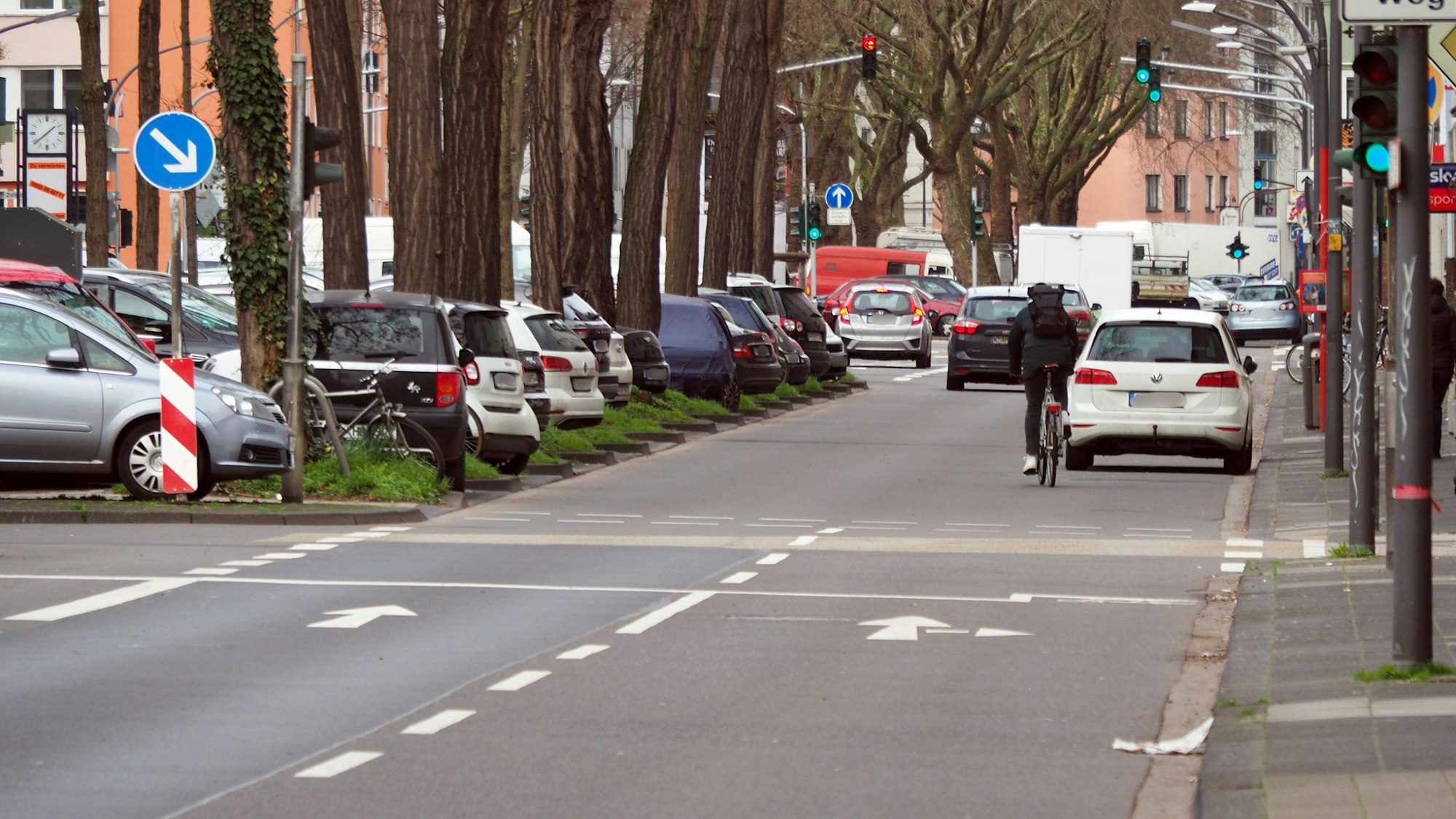 Blick auf eine zweispurige Straße mit Mittelallee. Dort parken viele Autos.