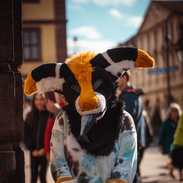 Eine 19-Jährige steht in einer Fußgängerzone und trägt eine plüschige Maske. Im Maul befindet sich ein Fisch aus Stoff.