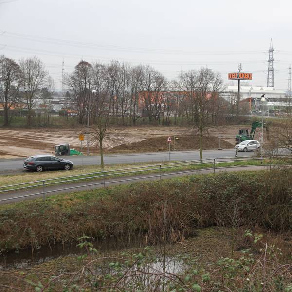 Eine Straße vor einem großen Baufeld mit grünen Baggern.