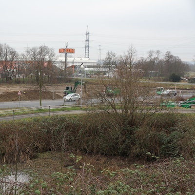 Eine Straße vor einem großen Baufeld mit grünen Baggern.