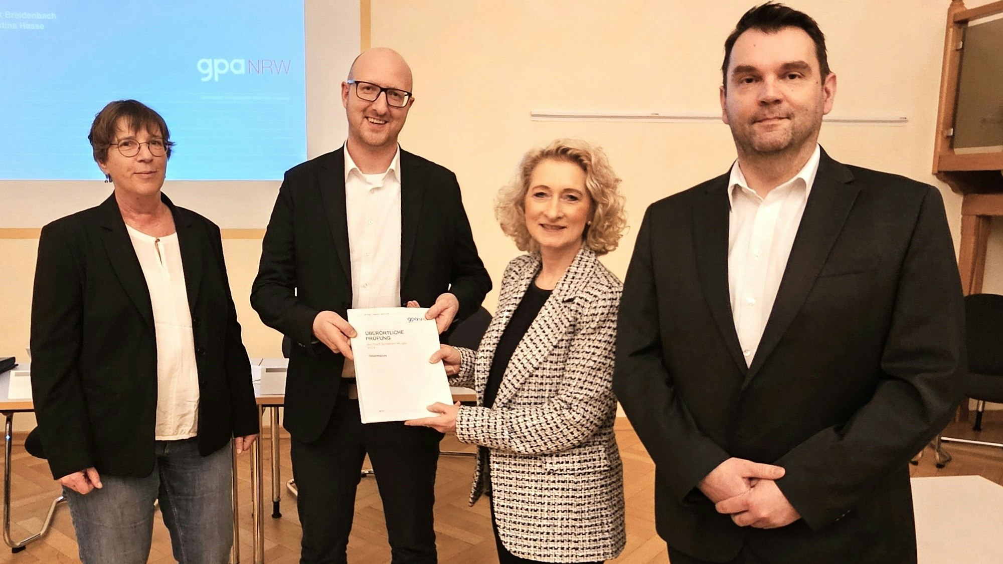 Christina Hasse, Ingo Pfennings, Simone Kaspar und Projektleiter Frank Breidenbach stehen nebeneinander und Kaspar überreicht dem Bürgermeister den Bericht.