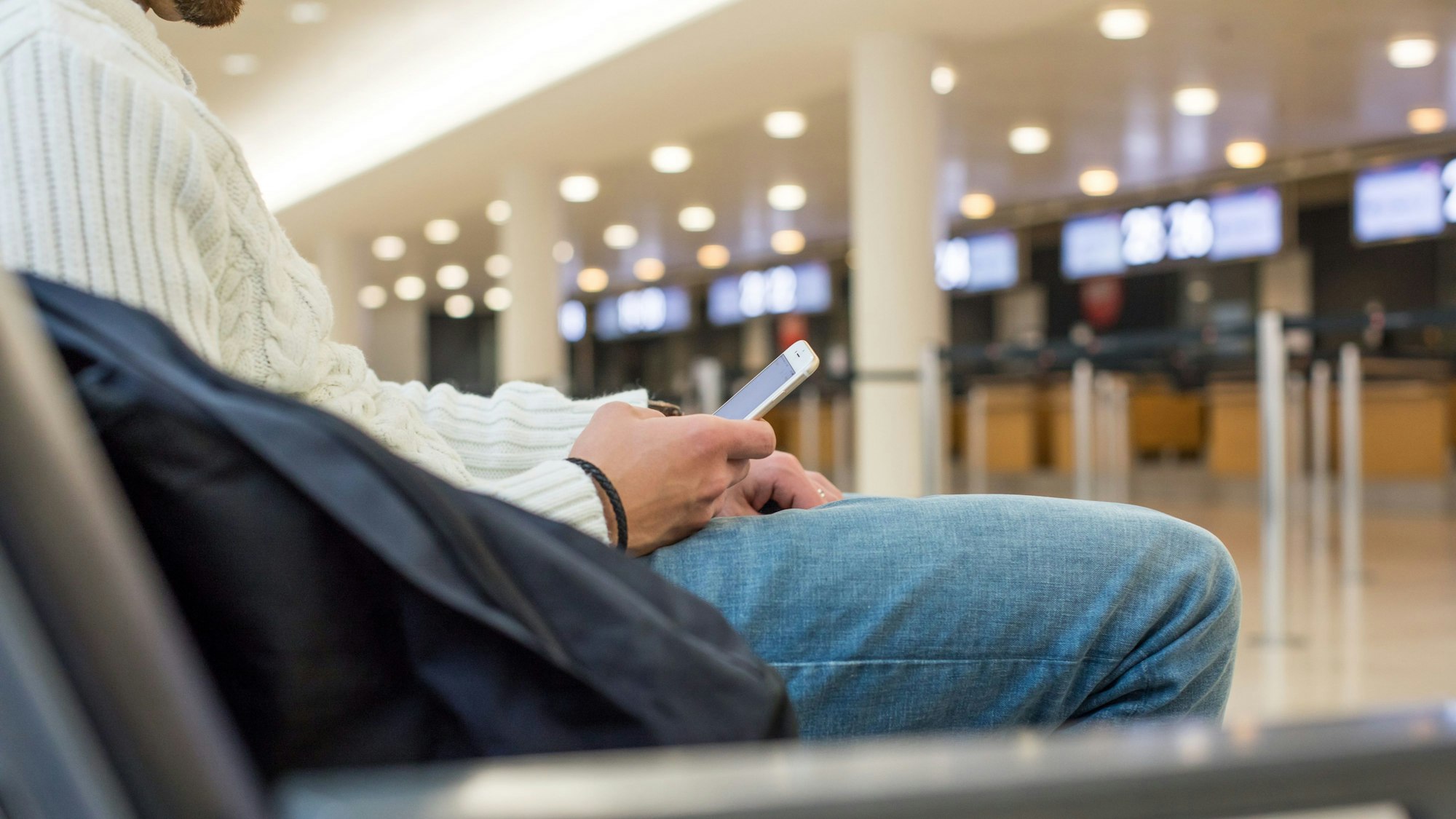 Ein Mann sitzt am Flughafenterminal mit einem Smartphone in der Hand