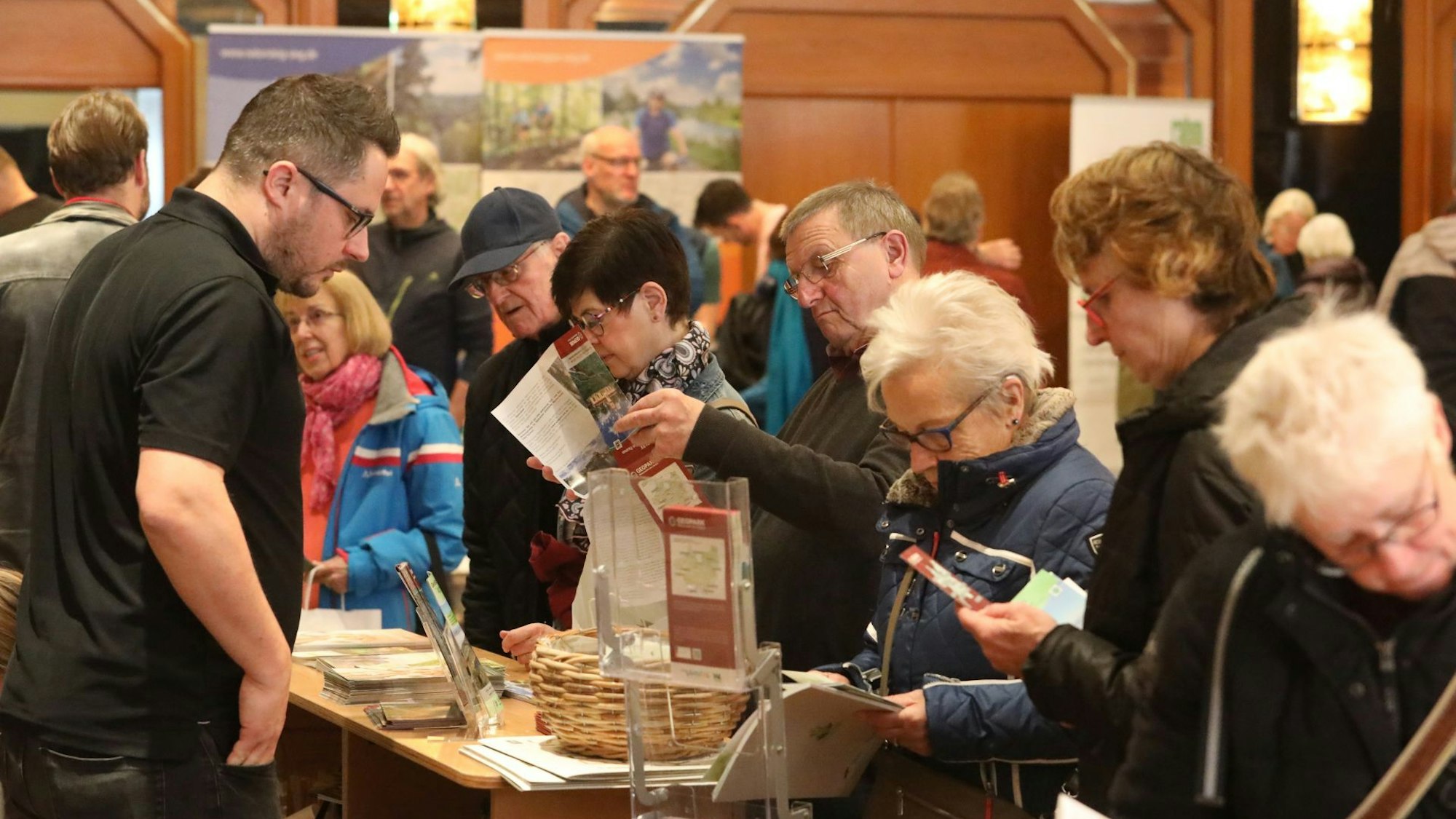 Männer und Frauen blättern an einem Messestand in Broschüren.