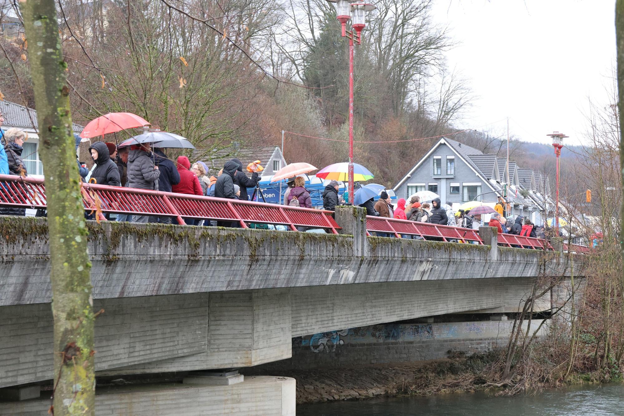 Auf einer Brücke stehen Menschen mit Regenschirmen.