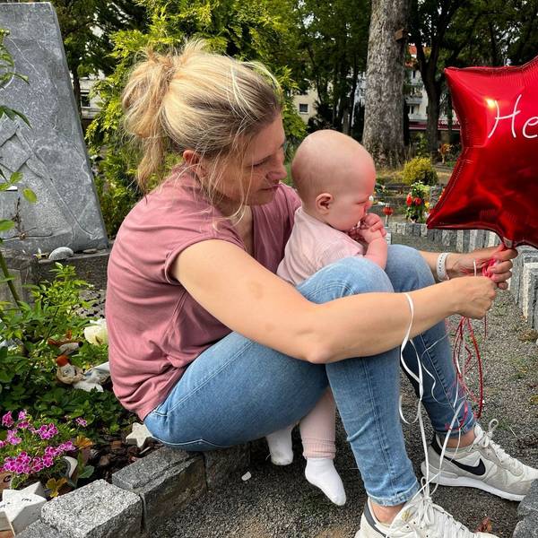 Das Bild zeigt Sarah Lenz mit Jana am Grab von Helen. Sie haben einen roten Ballon in der Hand.