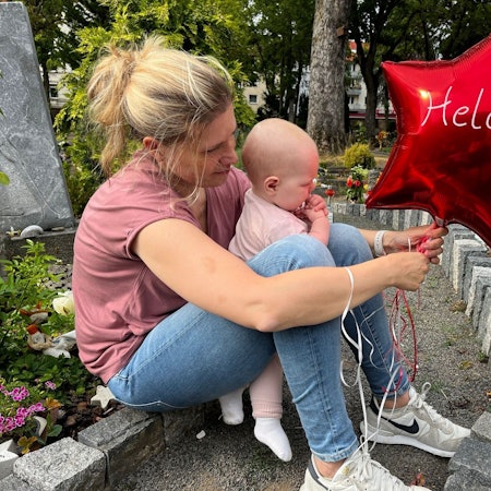 Das Bild zeigt Sarah Lenz mit Jana am Grab von Helen. Sie haben einen roten Ballon in der Hand.