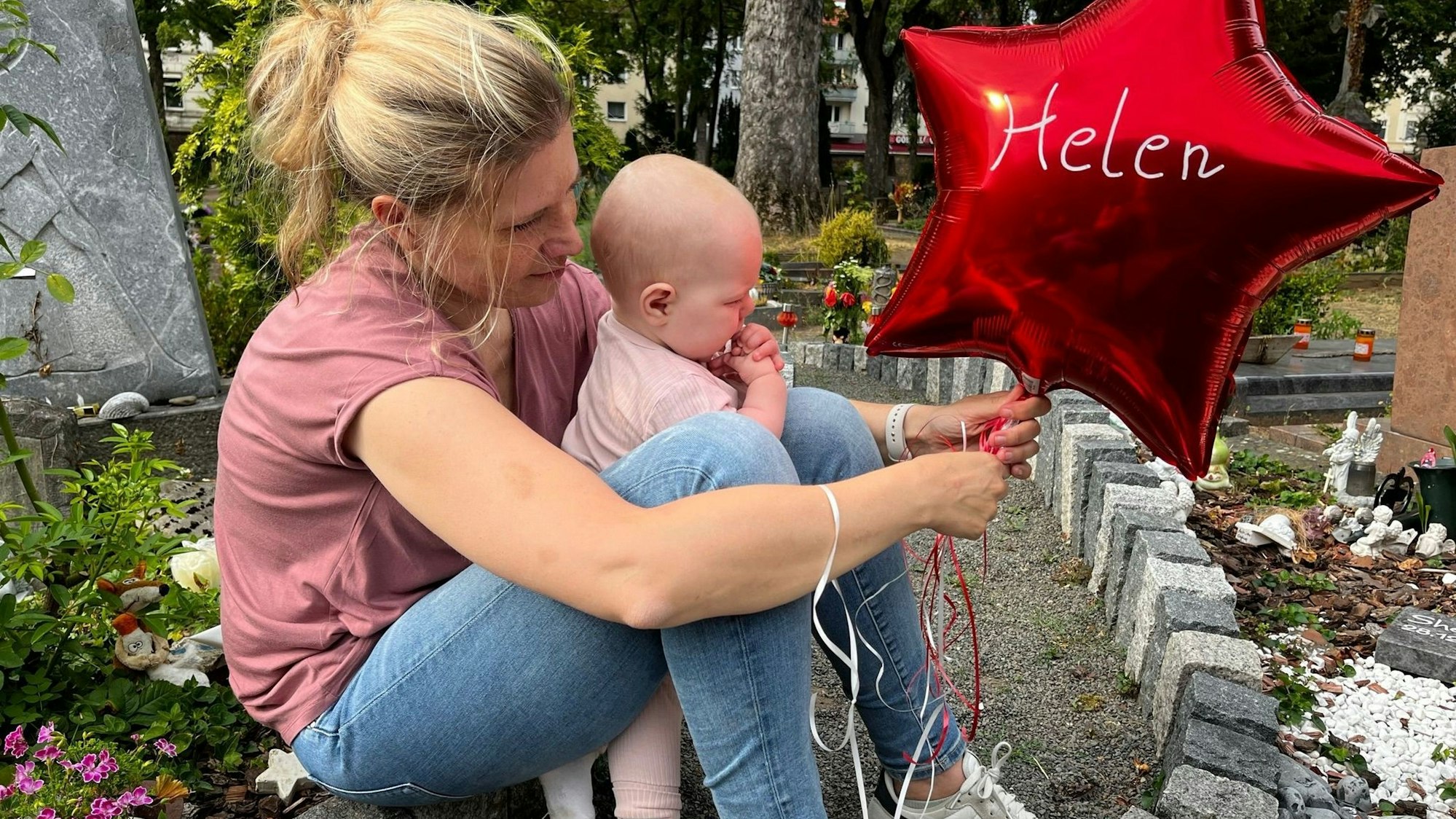 Das Bild zeigt Sarah Lenz mit Jana am Grab von Helen. Sie haben einen roten Ballon in der Hand.