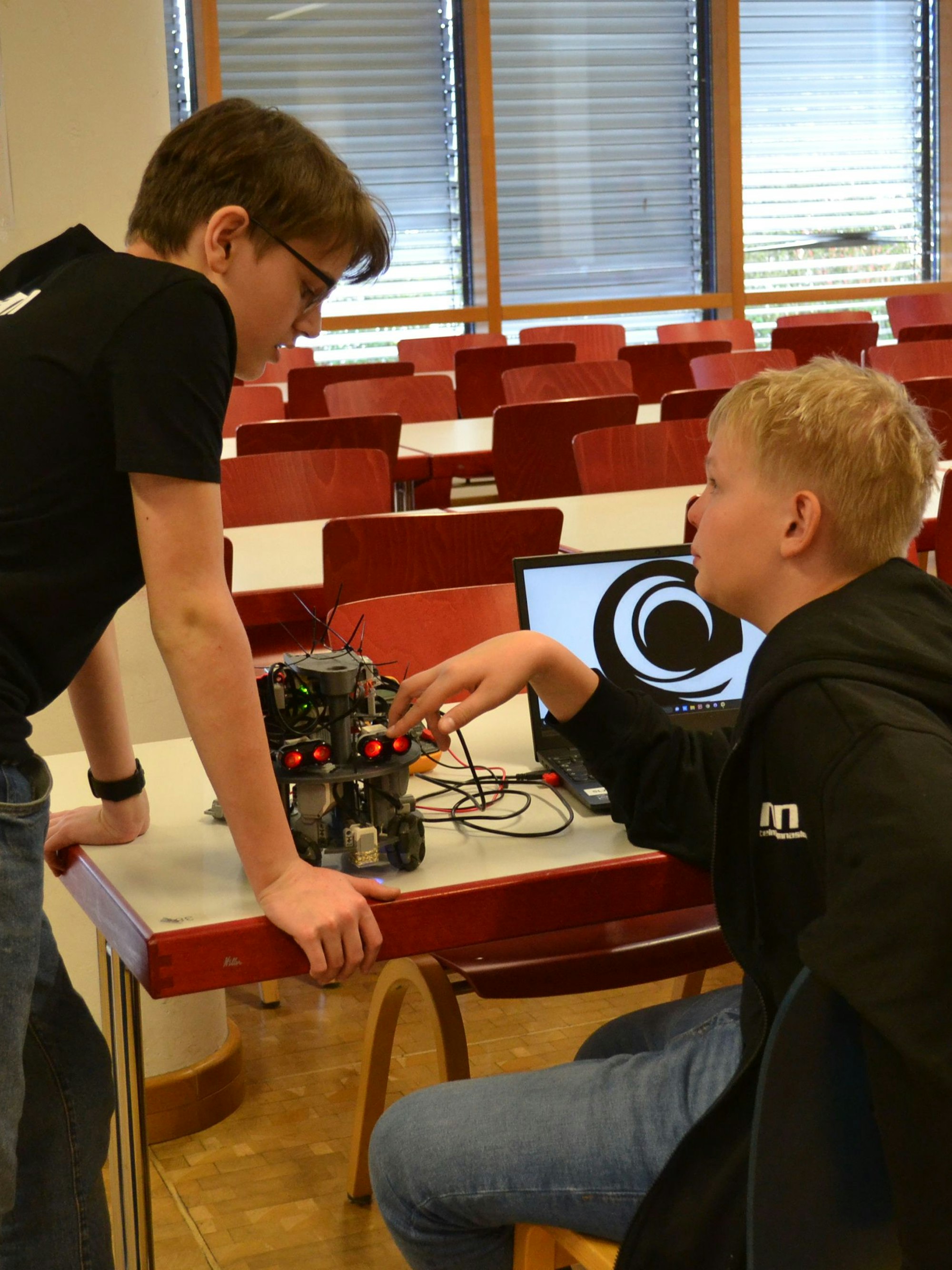 Zwei Jungen im Gespräch. Auf einem Tisch steht ein fahrbarer Roboter.