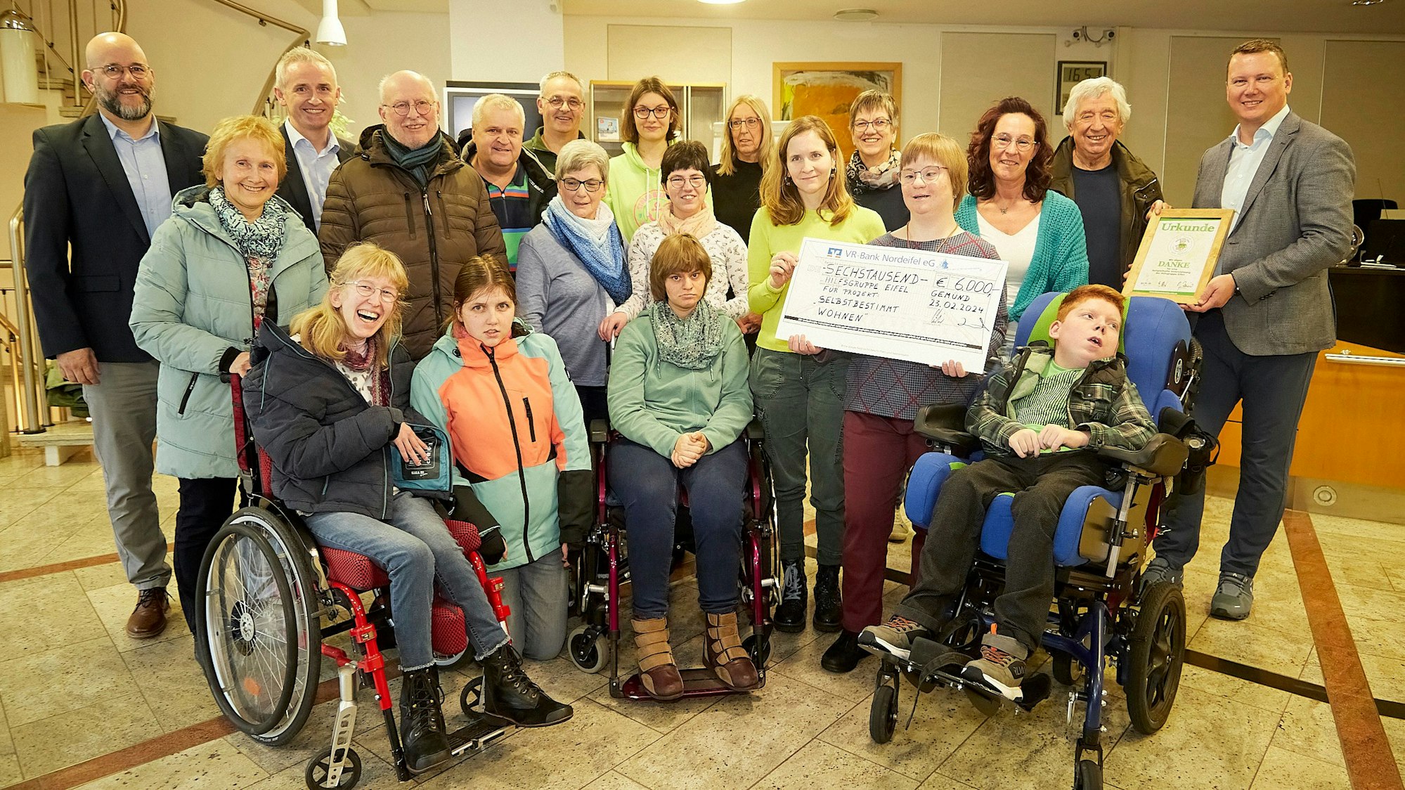 Eine Gruppe von Menschen mit Beeinträchtigungen posieren für ein Foto. Zwei von ihnen halten einen Scheck.