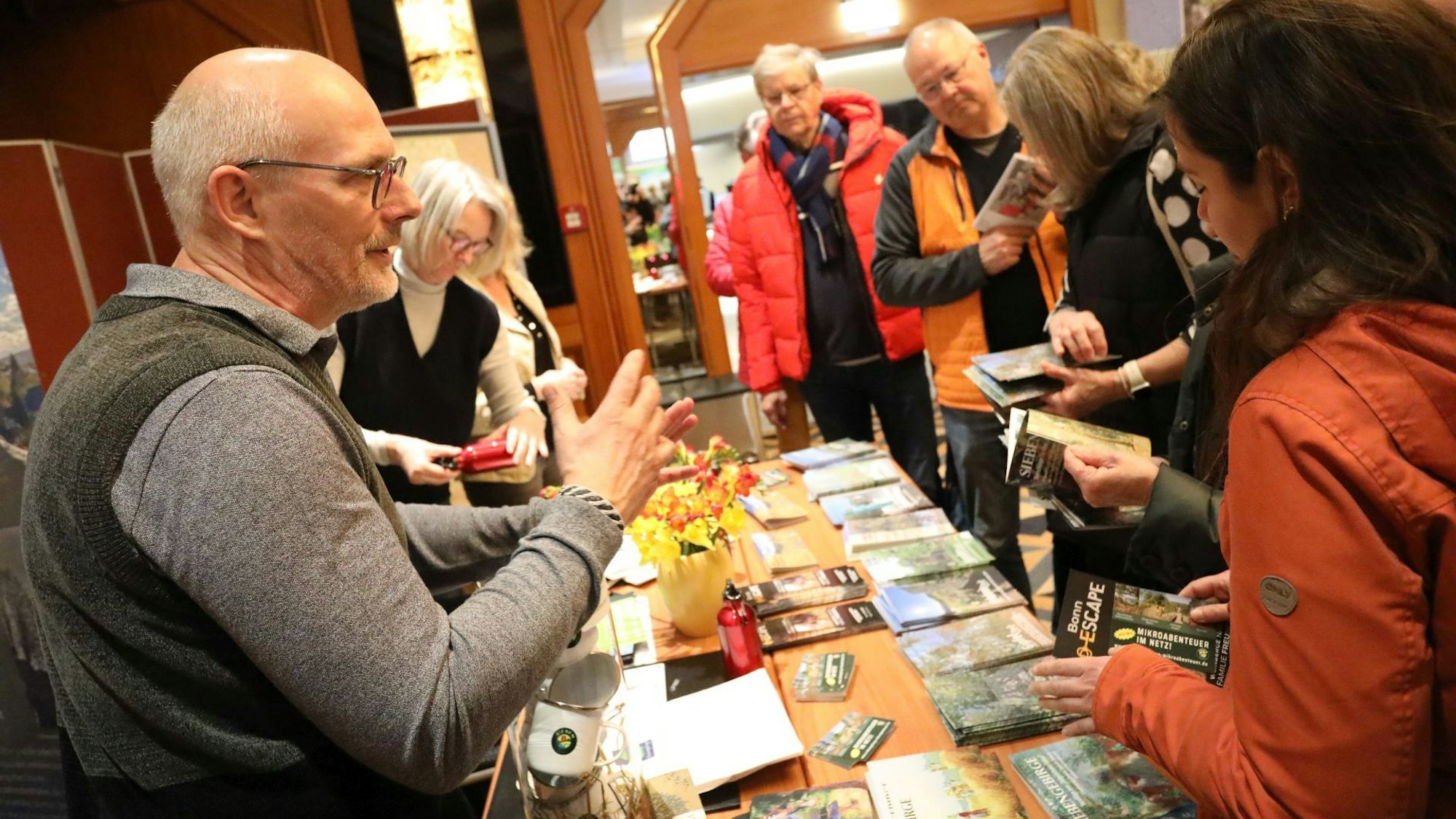 Ein Mann mit Bart und Brille spricht mit Besuchern eines Messestandes. Die Besucher tragen Outdoor-Kleidung.