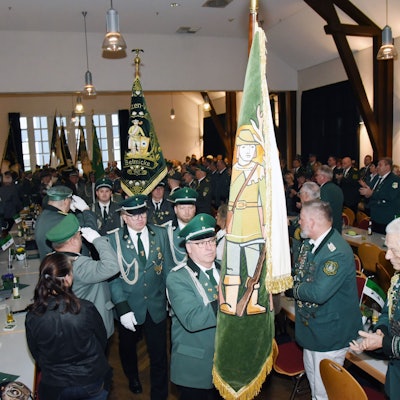 Männer in grünen Uniformen tragen Fahnen in einen Saal.
