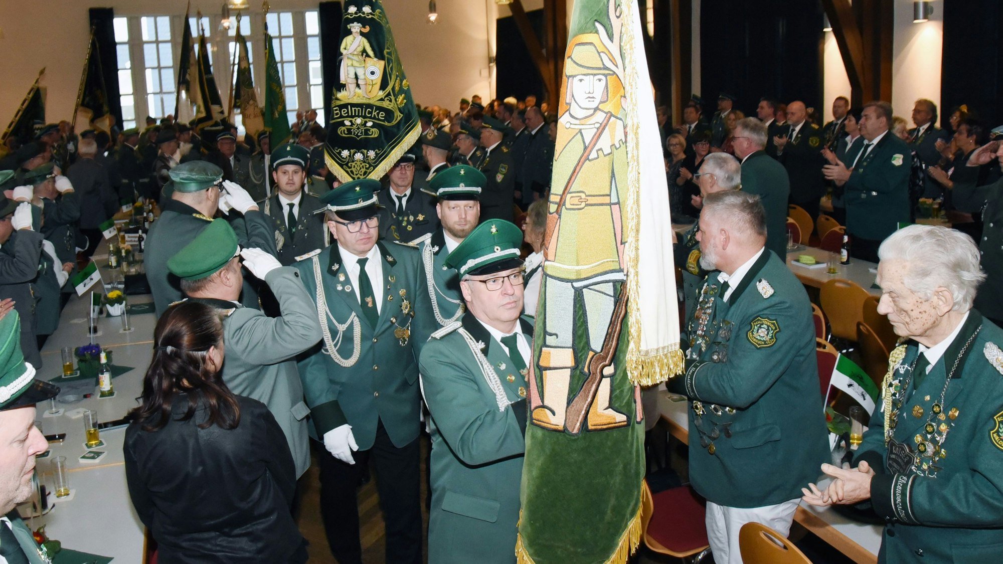 Männer in grünen Uniformen tragen Fahnen in einen Saal.