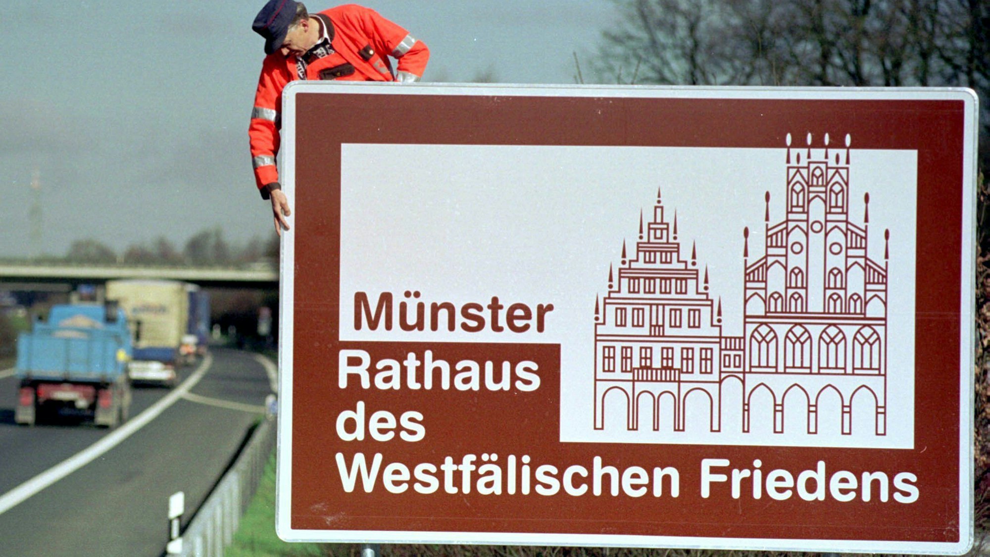 ARCHIV - 08.03.1998, Nordrhein-Westfalen, Münster: Ein Straßenobermeister überprüft im März 1998 auf der Autobahn A1 zwischen Ahaus und Münster das damals frisch aufgestellte Hinweisschild auf das Rathaus des Westfälischen Friedens in Münster.