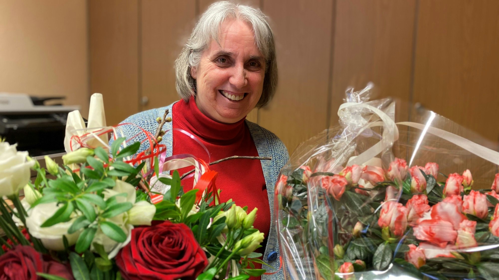 Pfarrerin Renate Kalteis sitzt zwischen zwei Blumensträußen.