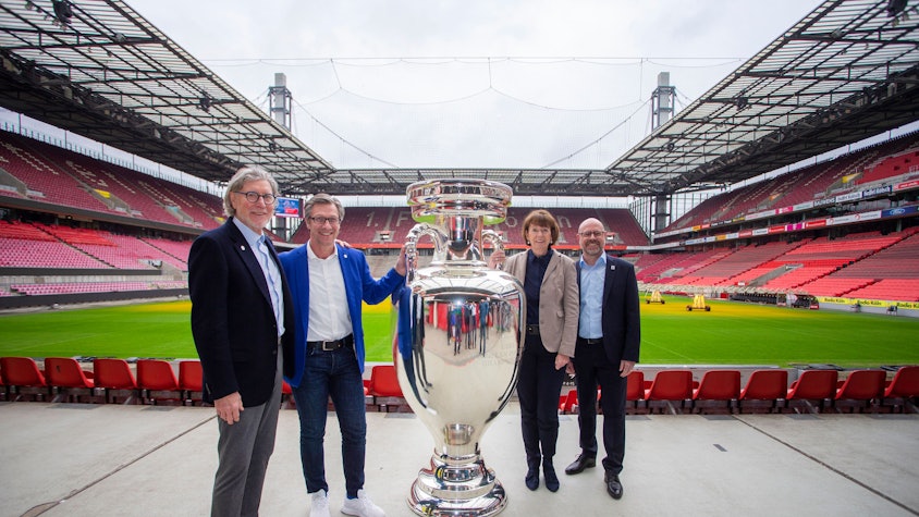Das Größte: Die Fußball-EM überstrahlt das Kölner Sportjahr. Vorfruede herrscht bereits bei EM-Botschafter Toni Schumacher, Christos Katzidis (Präsident des Fußball-Verbandes Mittelrhein), Oberbürgermeisterin Henriette Reker und Sportstätten-Chef Lutz Wingerath. Die Personen stehen mit riesiger EM-Pokal-Attrappe im Rheinenergie-Stadion.