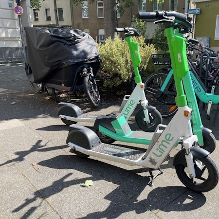 Mehrere E-Scooter stehen auf einem Gehweg.