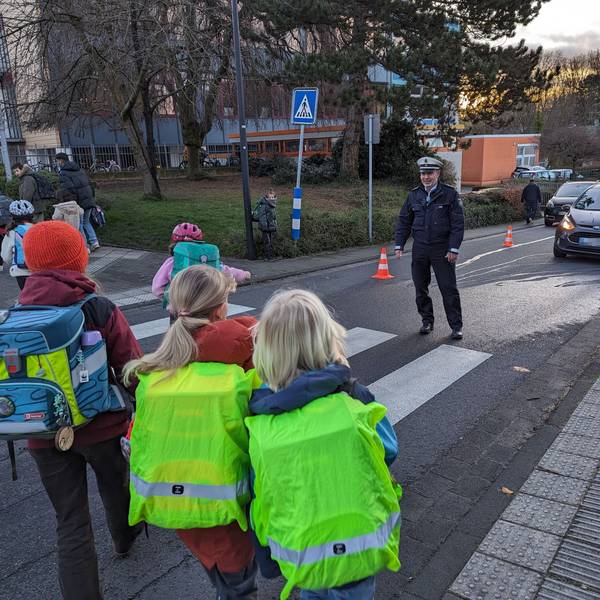 Schulkinder gehen im Beisein eines Polizisten über einen Zebrastreifen.