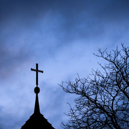 ARCHIV - 25.01.2024, Niedersachsen, Hannover: Dunkle Wolken ziehen über das Kreuz auf einer evangelischen Kirche in der Region Hannover hinweg