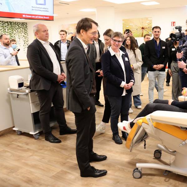 Einige Menschen stehen bei einer Frau, die auf einer Liege sitzt und Blutplasma spendet.