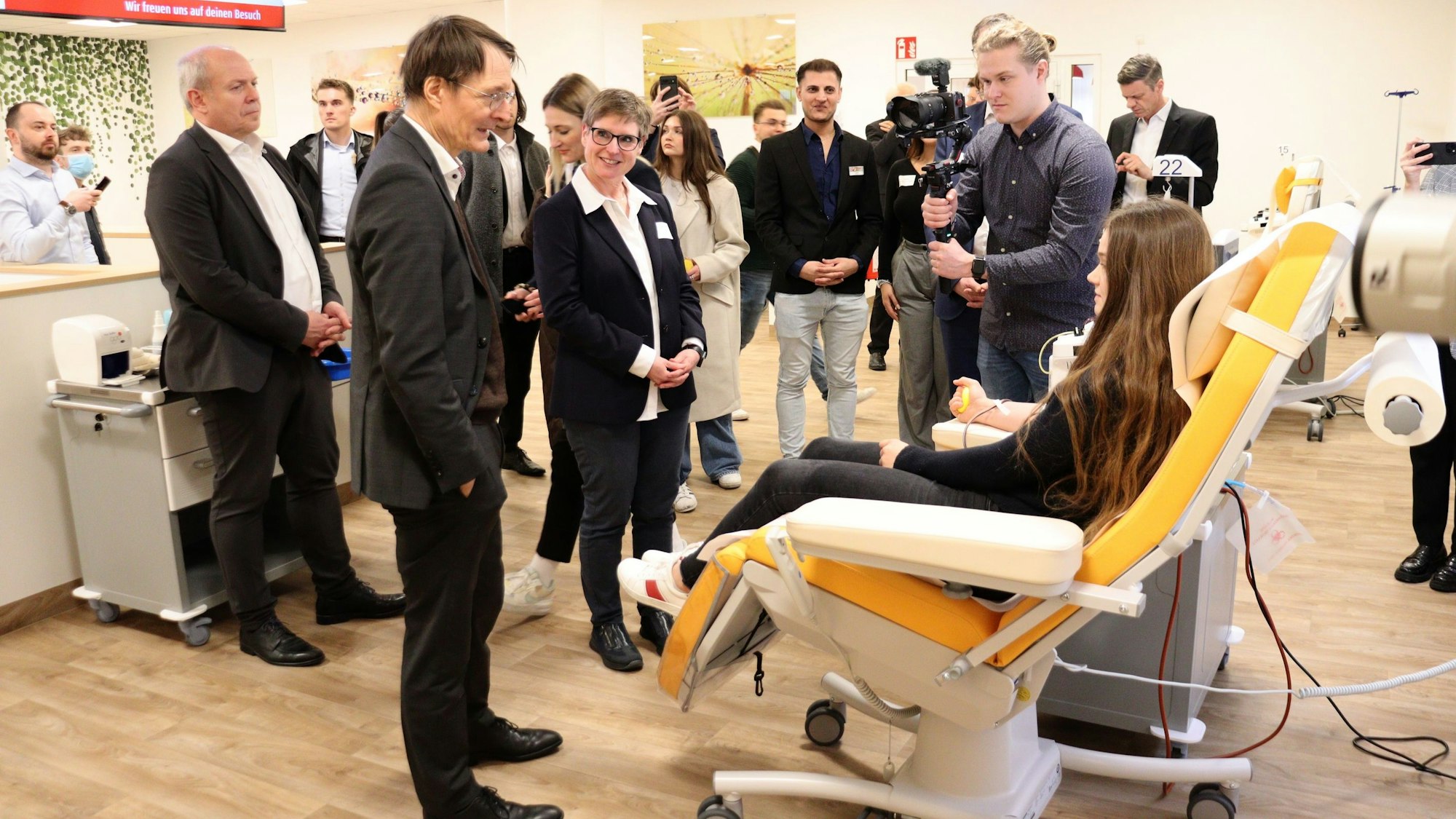 Einige Menschen stehen bei einer Frau, die auf einer Liege sitzt und Blutplasma spendet.