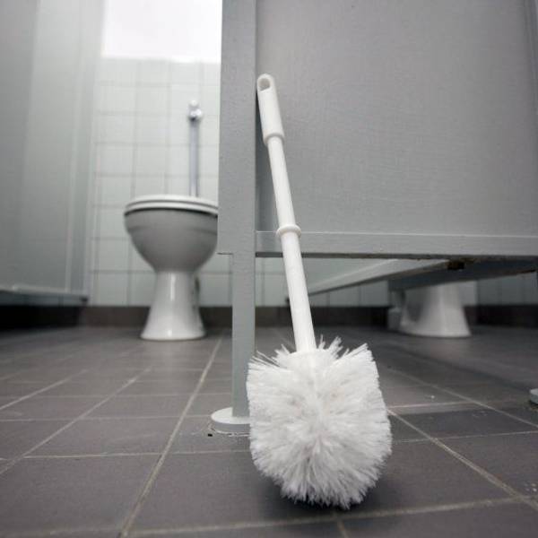 Eine Klobürste lehnt an einer Tür in Toilettentrakt.
