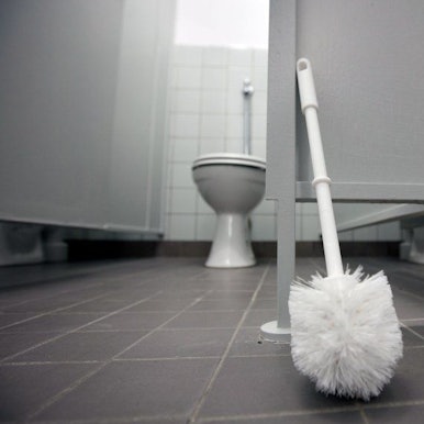 Eine Klobürste lehnt an einer Tür in Toilettentrakt.