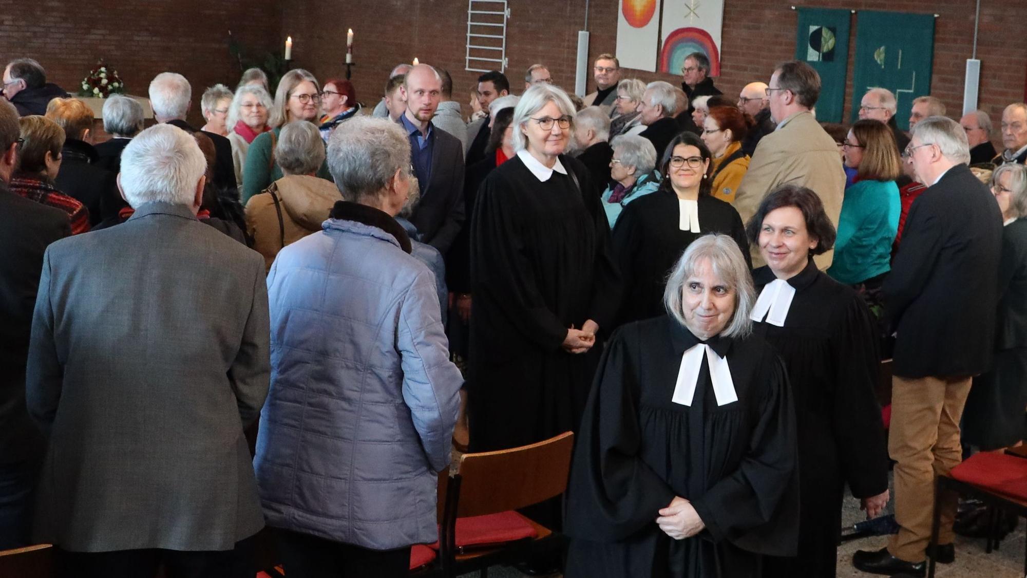 Pfarrerin Renate Kalteis und Gemeindesekretärin Elke Bell verlassen im Talar die Kirche. Die Menschen haben sich während des Gottesdienstes von ihren Plätzen erhoben.