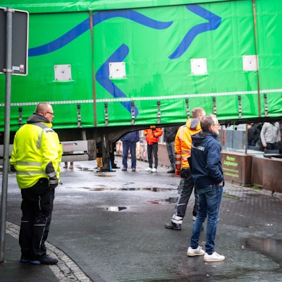Das Bild zeigt, wie der Auflieger von einem Krank angehoben wird. Mehrere Menschen schauen sich das Spektakel an.