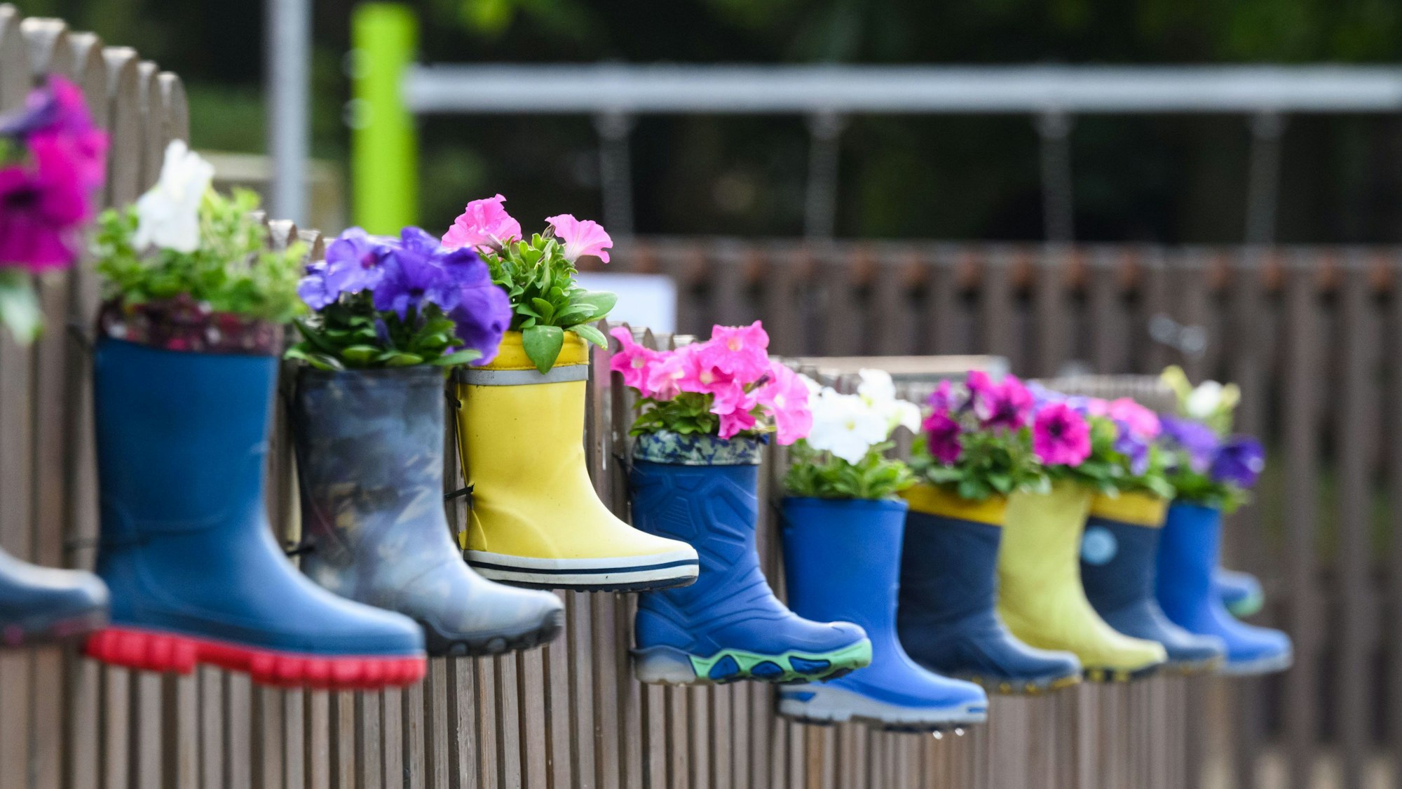 Gummistiefel von Kindern mit Blumen hängen am Zaun eines Kindergartens (Symbolbild)