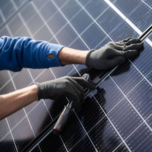Ein Mann montiert Photovoltaikmodule auf dem Dach eines Wohnhauses.