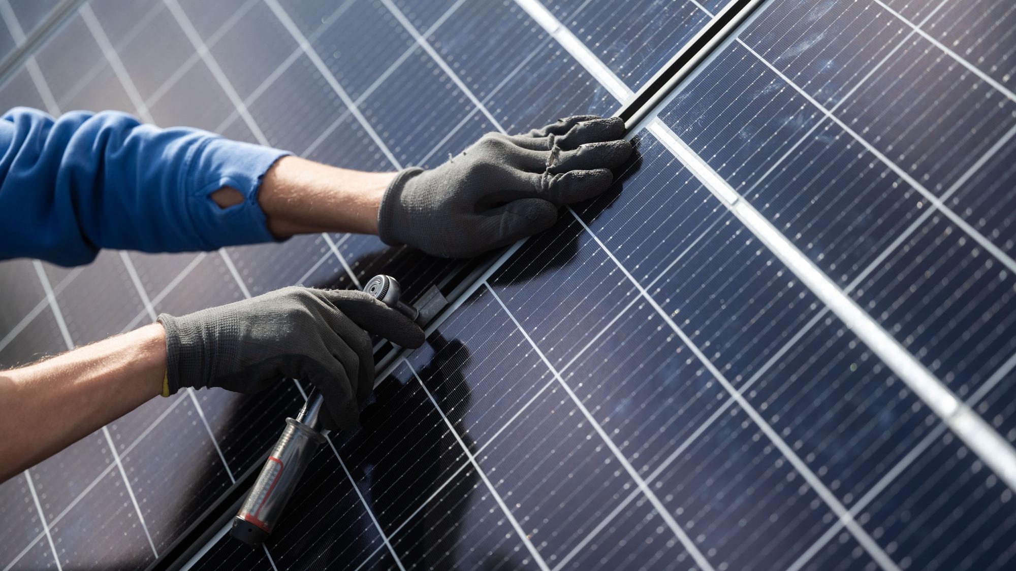 Ein Mann montiert Photovoltaikmodule auf dem Dach eines Wohnhauses.
